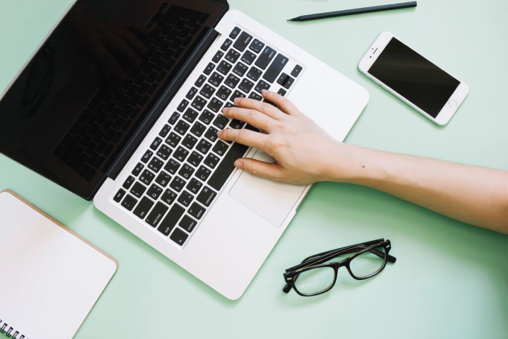 hand using laptop near smartphone glasses